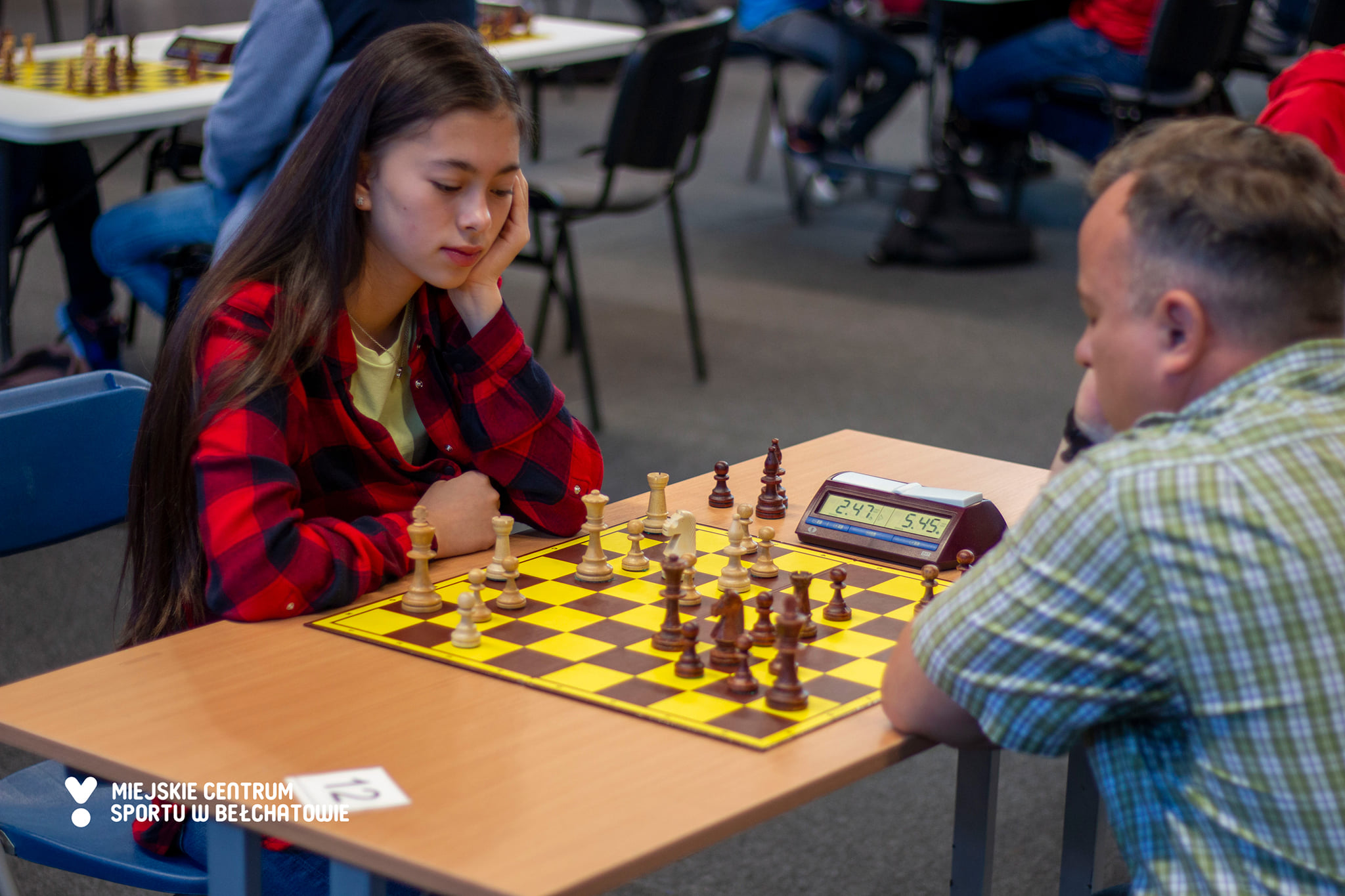 na zdjęciu znajduje się dziewczyna w czarno-czerwonej koszuli w kratę w trakcie gry w szachy na turnieju