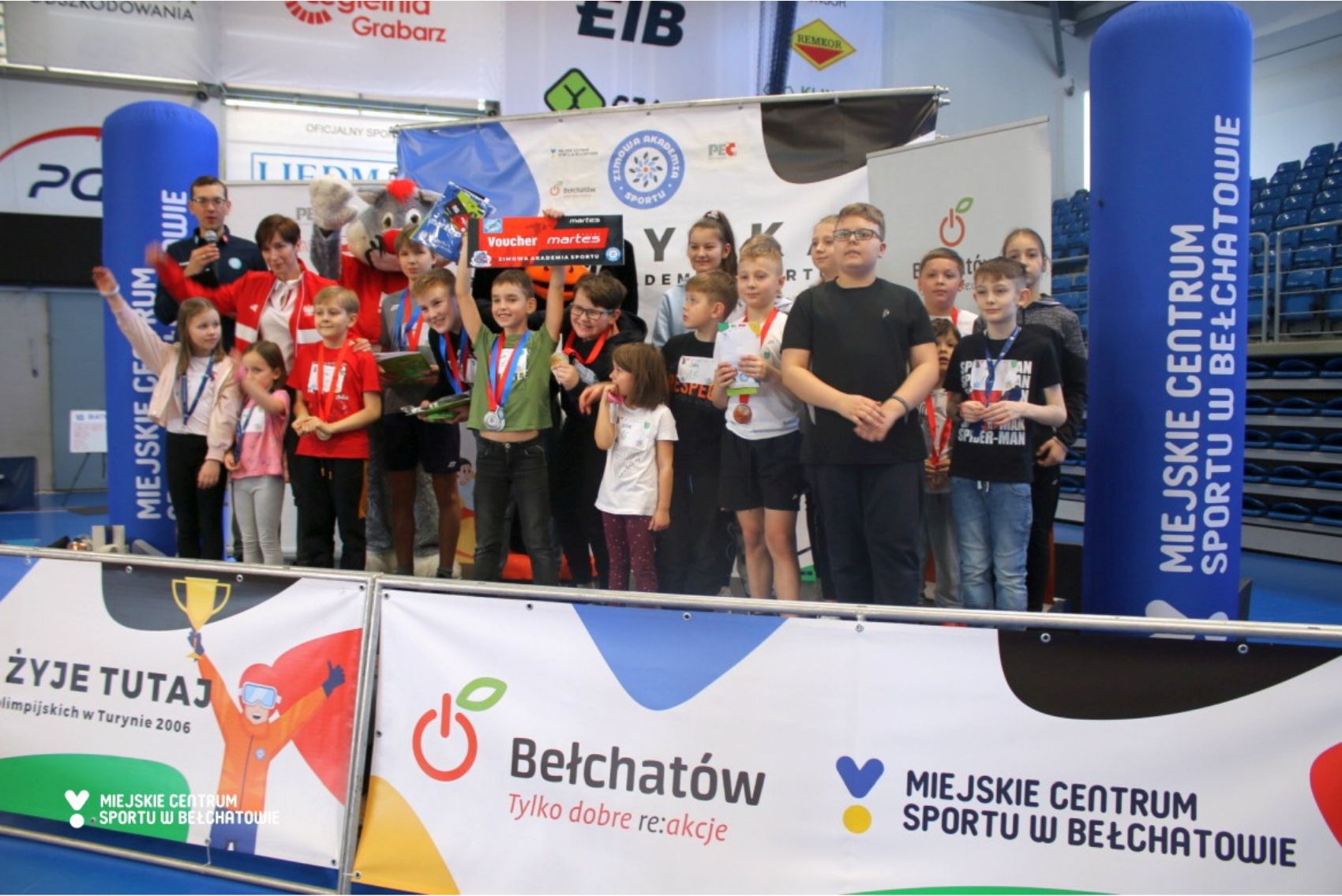 na zdjęciu widoczna na scenie grupa dzieci i organizatorów, które pozują do zdjęć z medalami i nagrodami w trakcie Festiwalu Sportów Zimowych - Igrzysk Zimowej Akademii Sportu